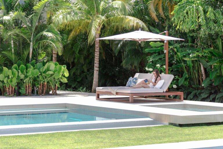 Sonnenliegen mit Sonnenschirm an einem Pool mit Grün im Hintergrund
