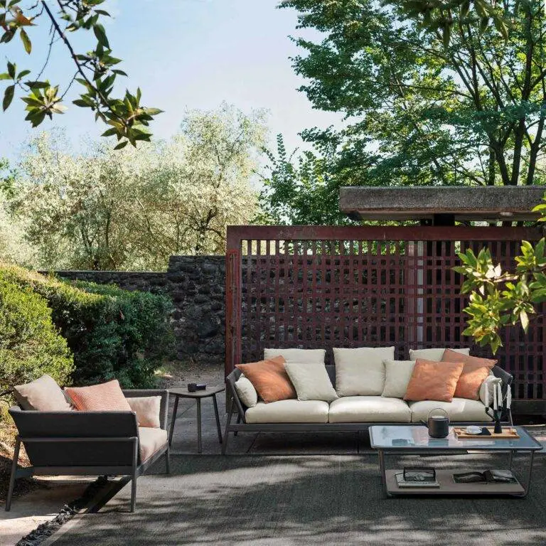 Große Sitzgarnitur mit Sofa und Stuhl stehen mit einem Tisch in einem Garten mit viel Grün im Schatten