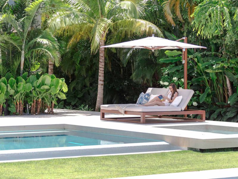 Sonnenliegen mit Sonnenschirm an einem Pool mit Grün im Hintergrund