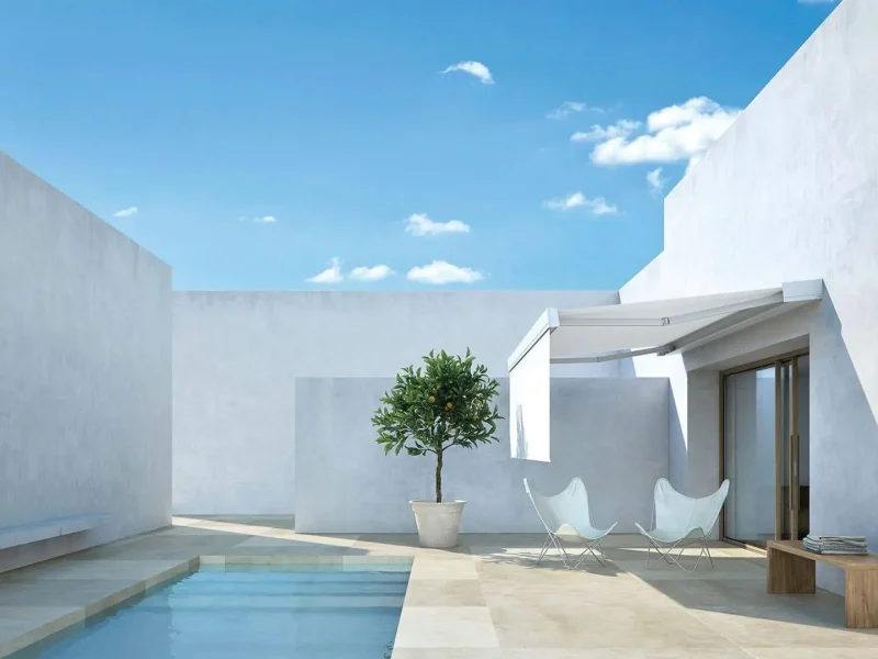 Helle, weiße Terrasse mit Pool und einem Bäumchen. Der Sitzbereich wird von einer weißen Markise beschattet.