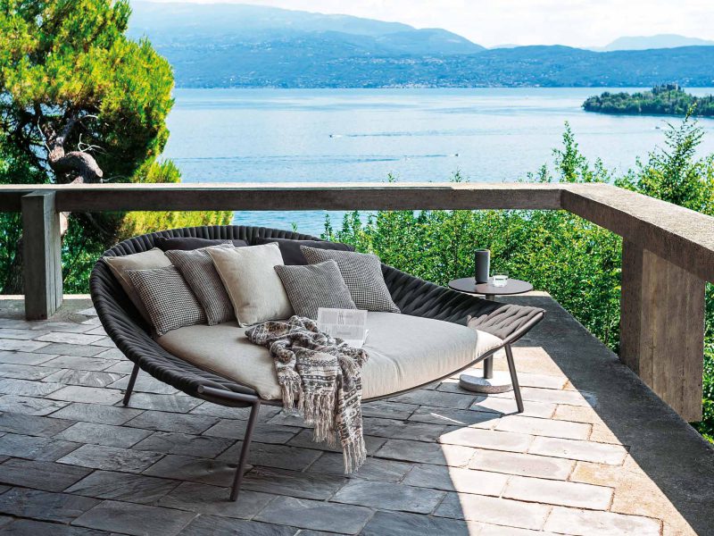 Outdoor-Sofa mit Kissen in der Farbe Grau und Beige auf der Terrasse. Strahlendes Wetter mit Blick auf das Meer.