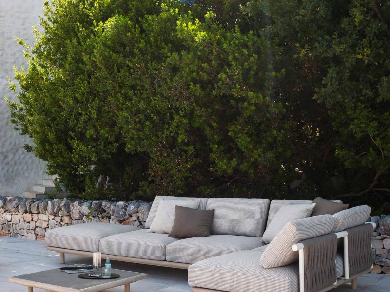 Gemütliches Sofa mit Tisch auf einer Terrasse im Schatten der Bäume.