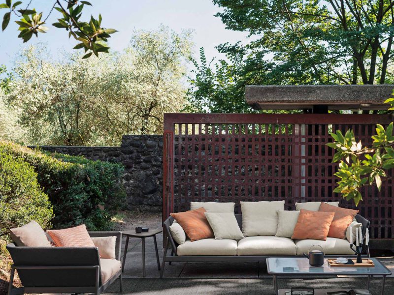 Große Sitzgarnitur mit Sofa und Stuhl stehen mit einem Tisch in einem Garten mit viel Grün im Schatten