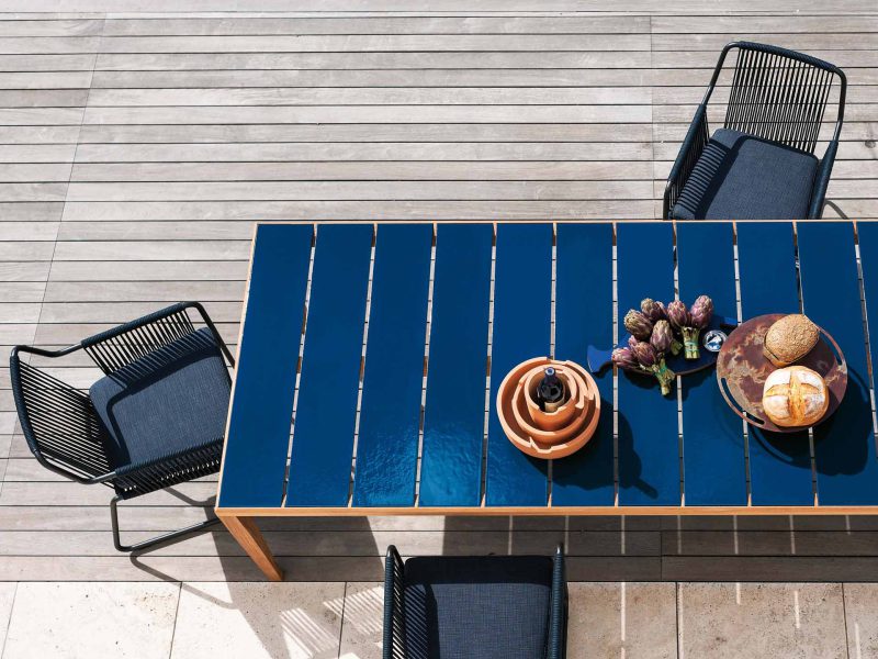 Blauer Gartentisch steht mit Stühlen am Rand des Pools.