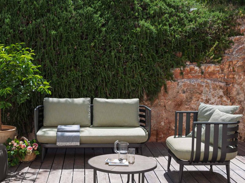 Couch, Sessel und Tisch auf einer Holzterrasse in der Sonne mit Bäumen im Hintergrund